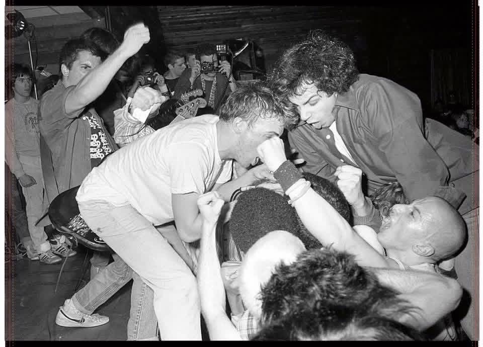 The crowd at the front of the stage at an SSD show, fists swinging and photographers leaning in.