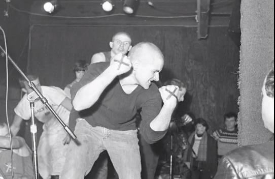 A dancer on stage at an SSD show swinging his fists with the crowd and microphone stands around him.