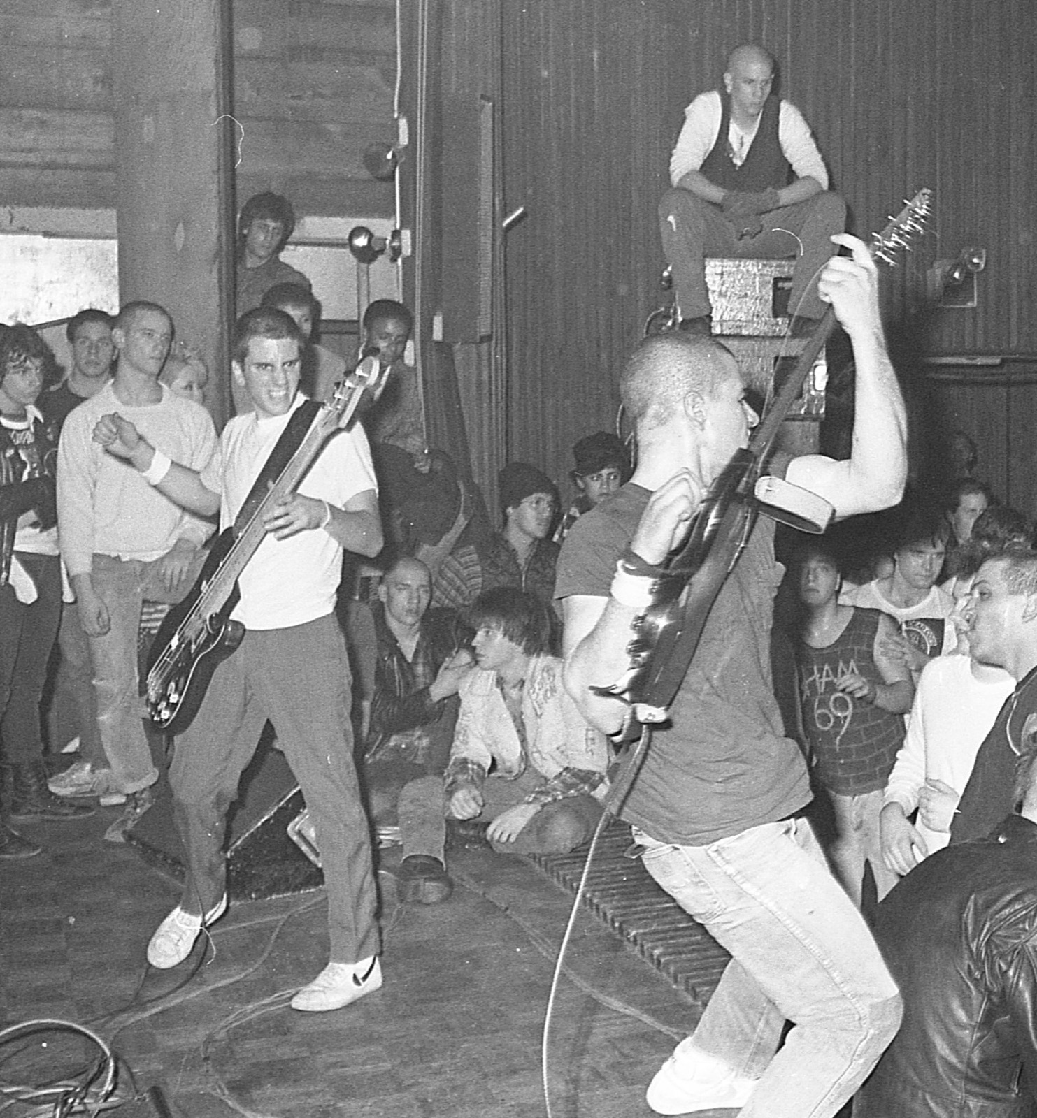 SSD playing surrounded by the crowd, a guitarist hoisting his guitar overhead while a fan looks on from the top of the speaker stack.