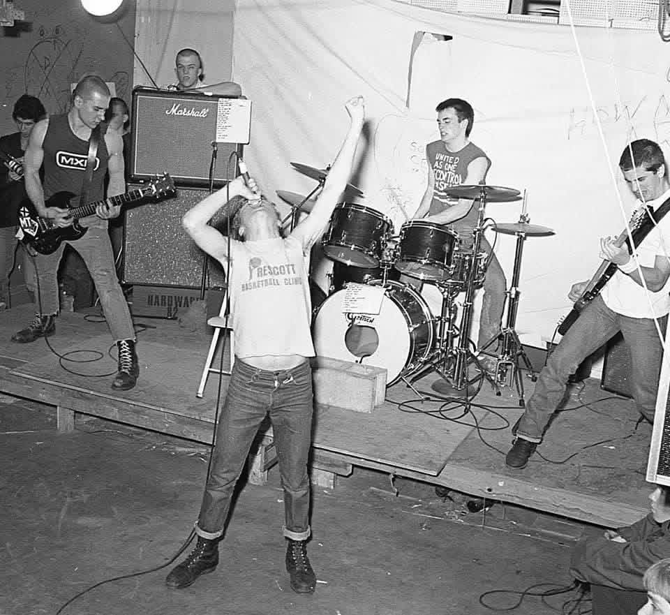 SSD playing live: singer Springa sings with his head thrown back at the microphone while the guitarists and drummer play behind him in front of a Marshall stack.