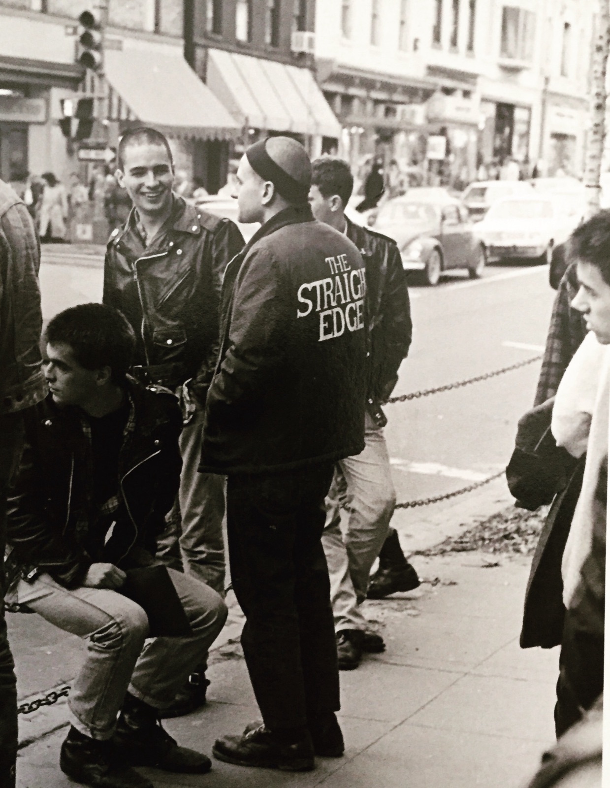 Members of the Boston Crew hanging out on a busy city sidewalk, one wearing a jacket printed with The Straight Edge.